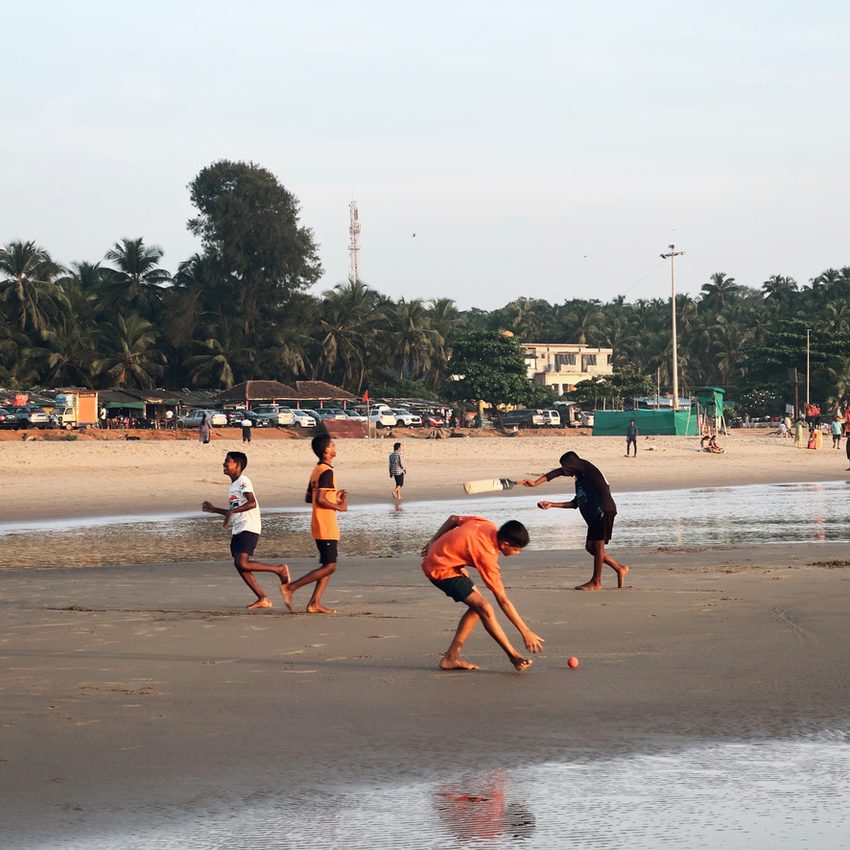 Children playing cricket on wet sand beside the sea.