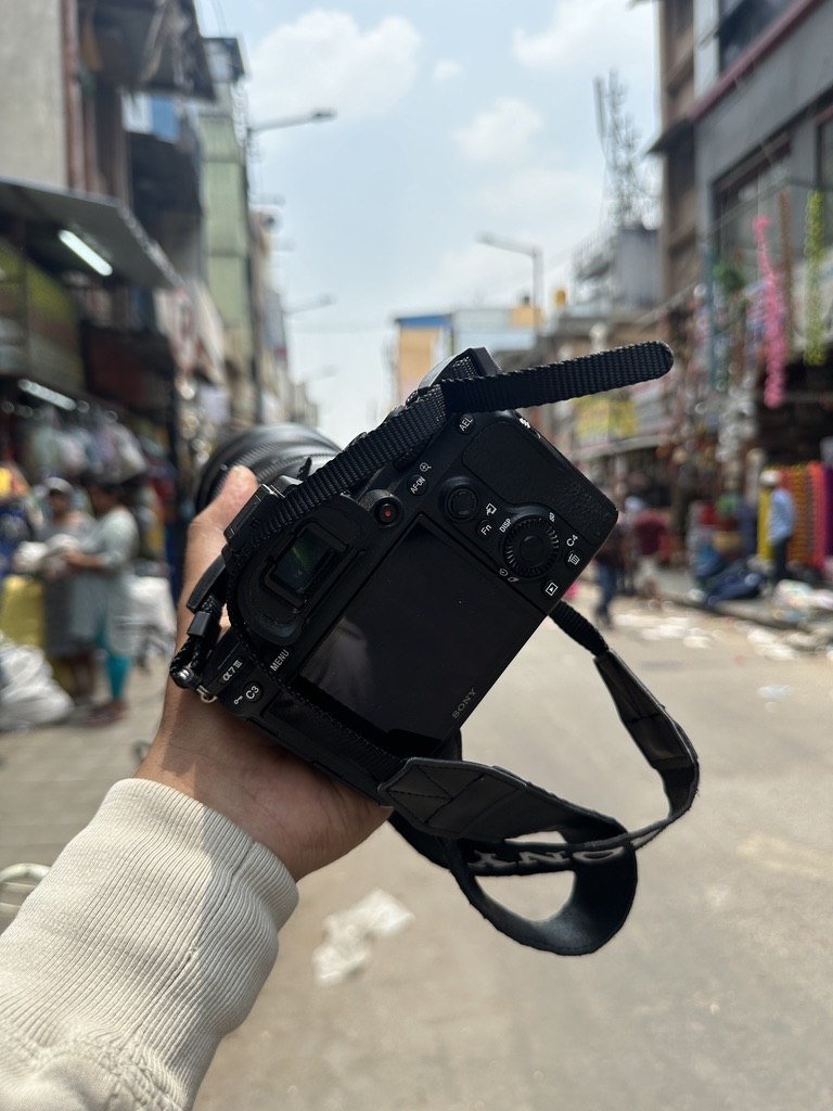 A Sony camera held in the foreground of a busy shopping street.
